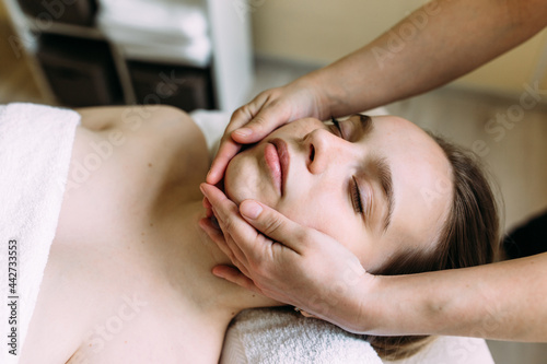 Masseur doing massage on a woman's face at the spa. © Zhuravleva Katia