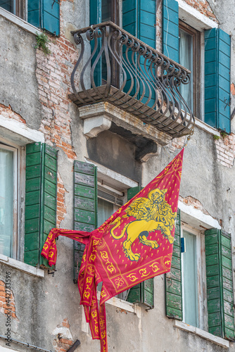 Old traditional city flag of Venice, Italy, depicting Venetian lion with wings and Bible hanging at very old deteriorated building facade. photo