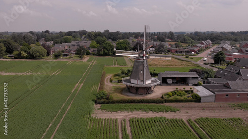 Green agriculture fields in Dutch landscape with a traditional windmill and village in the background. Aerial of countryside in The Netherlands