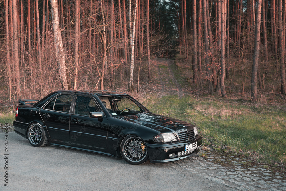 Goleniow, Poland - April 20th, 2021: Old black tuned Mercedes Benz C-class  (W202 model) near forest. Compact luxury sedan icon from the 90s. Side view  Stock Photo