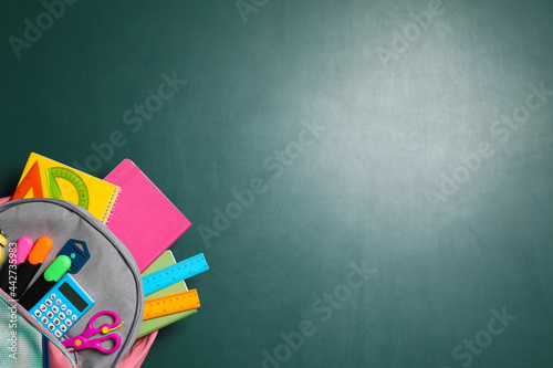 Backpack with different stationery on chalkboard background, top view. Space for text