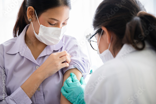 A female doctor or nurse wearing a mask  glove  and face shield are injecting the coronavirus 19 vaccine on the shoulder of the woman to immunize. Concept of preventing the spread of COVID-19.