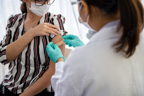 Female doctor or nurse stuck a plaster bandage  give with a young woman. After vaccination against coronavirus 19 for immunize. Concept of preventing the spread of COVID-19.