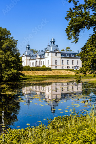 picturesque Kronovall Castle and gardens reflected in a pond in the foreground on a summer dday under a blue sky