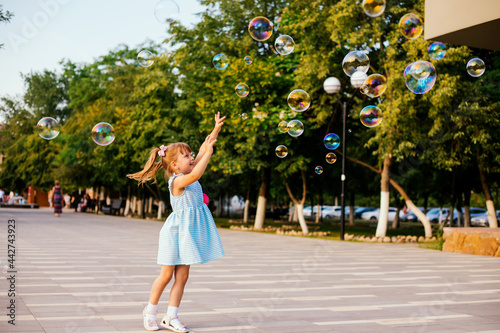 In a public park, a little girl blows and catches soap bubbles.The child is playing and laughing. © Cherkasova Alie