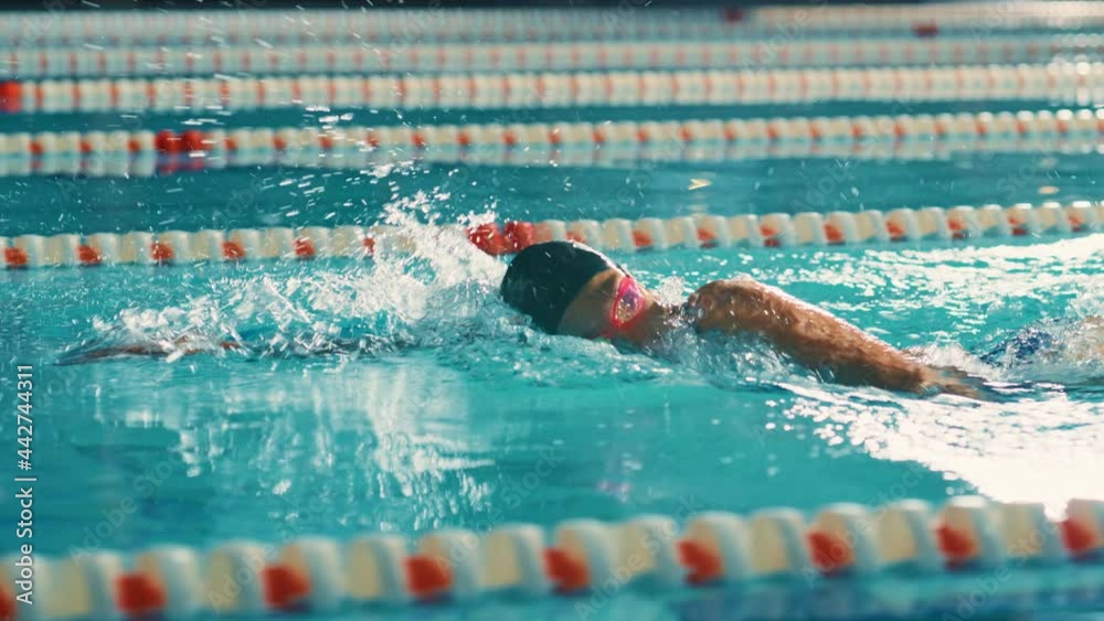 Successful Female Swimmer Racing in Swimming Pool. Professional Athlete Determined to Win Championship using Freestyle. Colorful Cinematic Shot. Side View Cinematic Tracking Shot