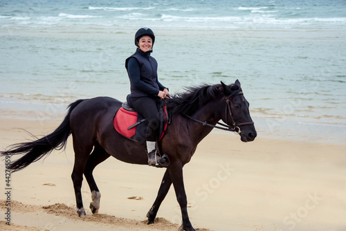 middle-aged woman riding a horse on the beach