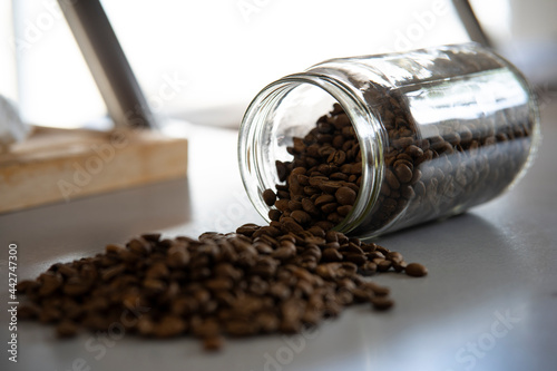 Bocal rempli de grains de café, renversé sur le plan de travail d'une cuisine. Vue de trois quart.