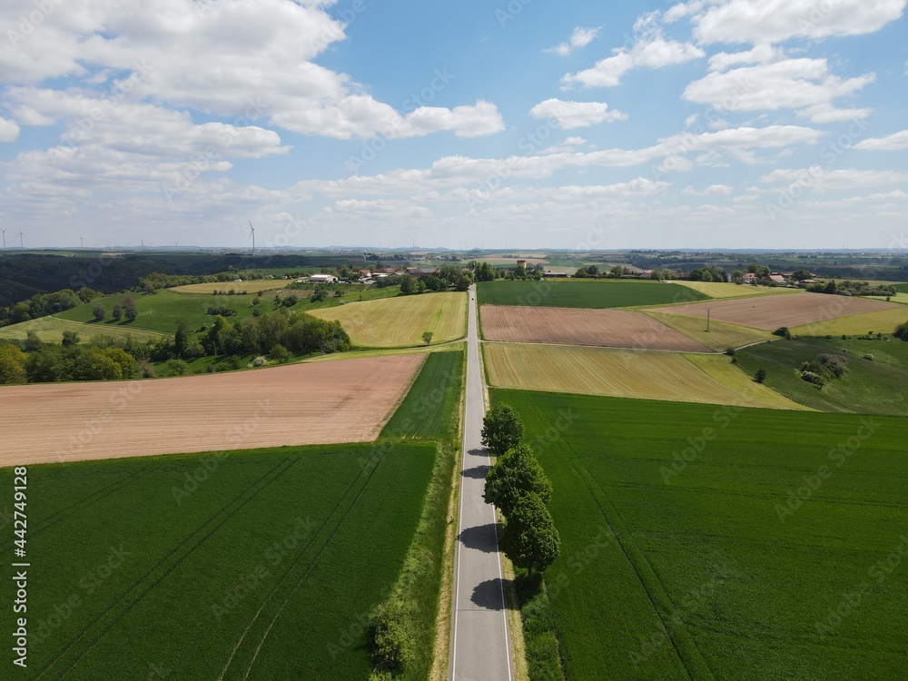 Aerial view of road between fields in the countryside with nice blue cloudy sky 