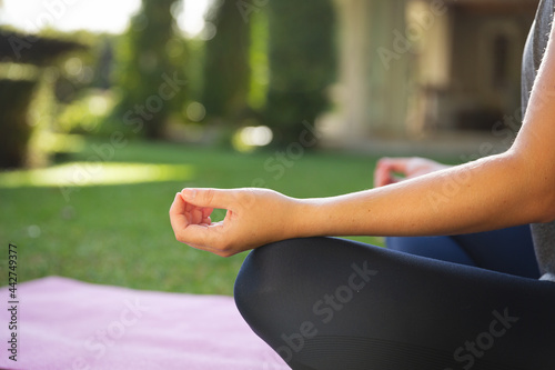 Midsection of caucasian woman practicing yoga in garden, sitting and meditating