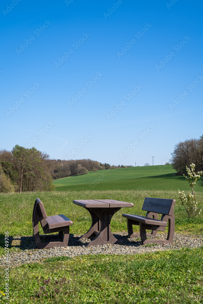 Brown table and benches to rest with grass hills and trees in the landscape