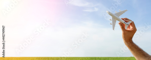 Flying plane on the blue sky banner background. A toy plane in hand flies to travel. Summer, vacation, travel, relaxation, tours and flights concept.