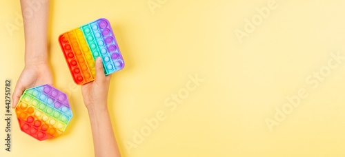 Kid toy banner background. Hands holding pop it fidget toys on yellow background. Top view, copy space photo