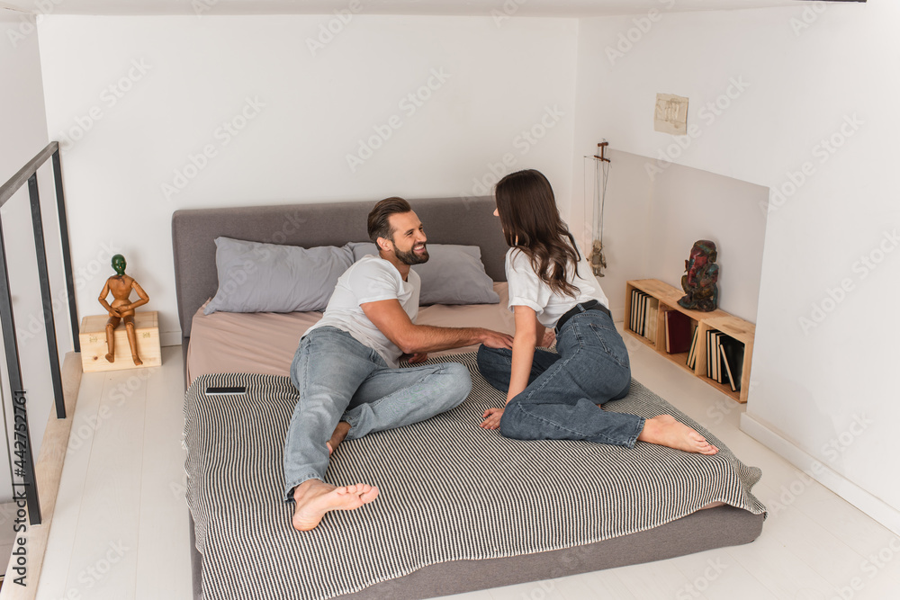 Smiling man lying on bed near girlfriend and smartphone