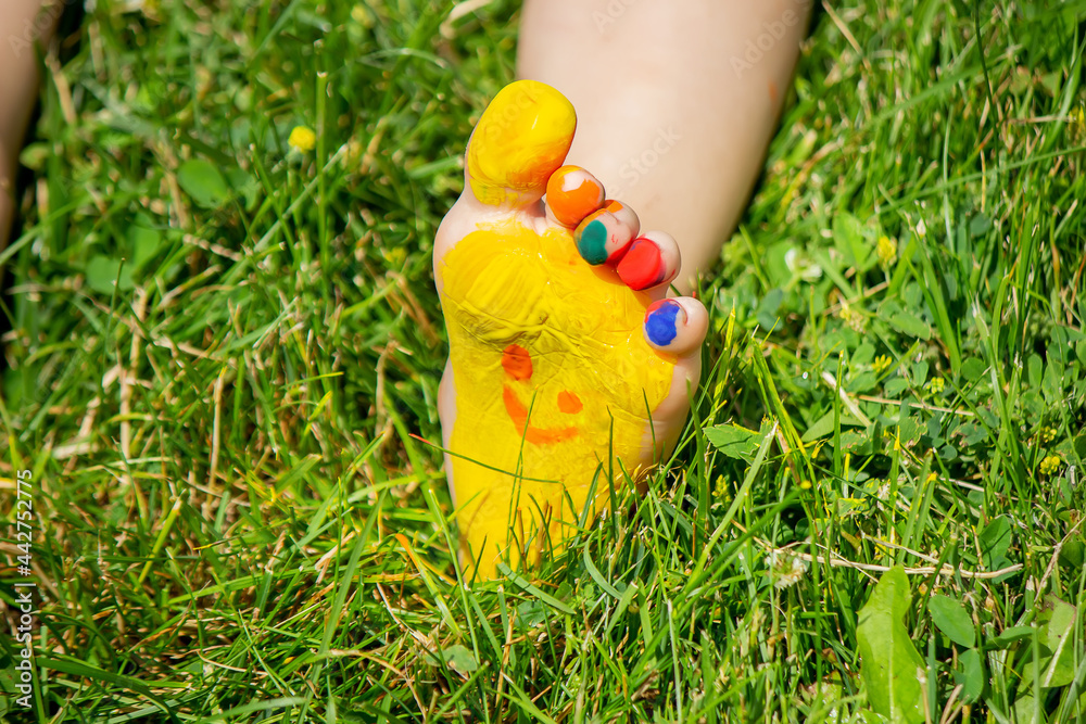 Fototapeta premium The child was lying on the green grass. Smile with paints on the legs and arms. Child having fun outdoors in the spring park. Selective focus.