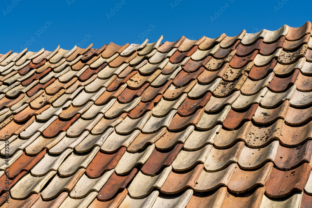 close up view of red and orange burned clay roof tiles undeer a clear blue sky close up view of red and orange burned clay roof tiles undeer a clear blue sky
