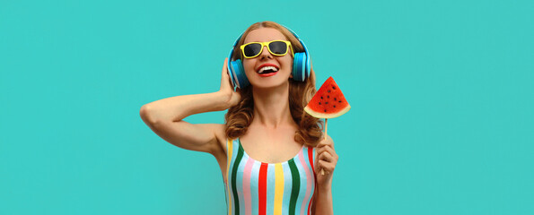 Summer colorful portrait of cheerful happy laughing young woman in headphones listening to music with juicy lollipop or ice cream shaped slice of watermelon on blue background