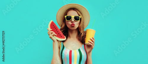 Summer colorful portrait of beautiful young woman blowing her lips with slice of watermelon and cup of juice wearing a straw hat on blue background
