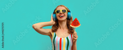 Summer colorful portrait of cheerful happy laughing young woman in headphones listening to music with juicy lollipop or ice cream shaped slice of watermelon on blue background