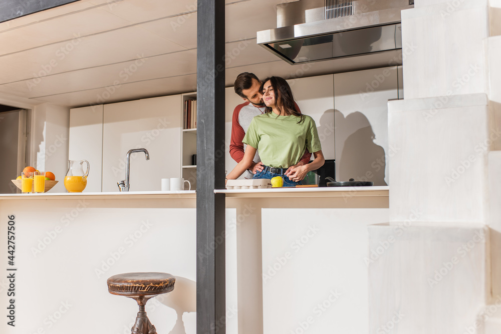 Man kissing girlfriend near orange juice and fruits in kitchen Man kissing girlfriend near orange juice and fruits in kitchen