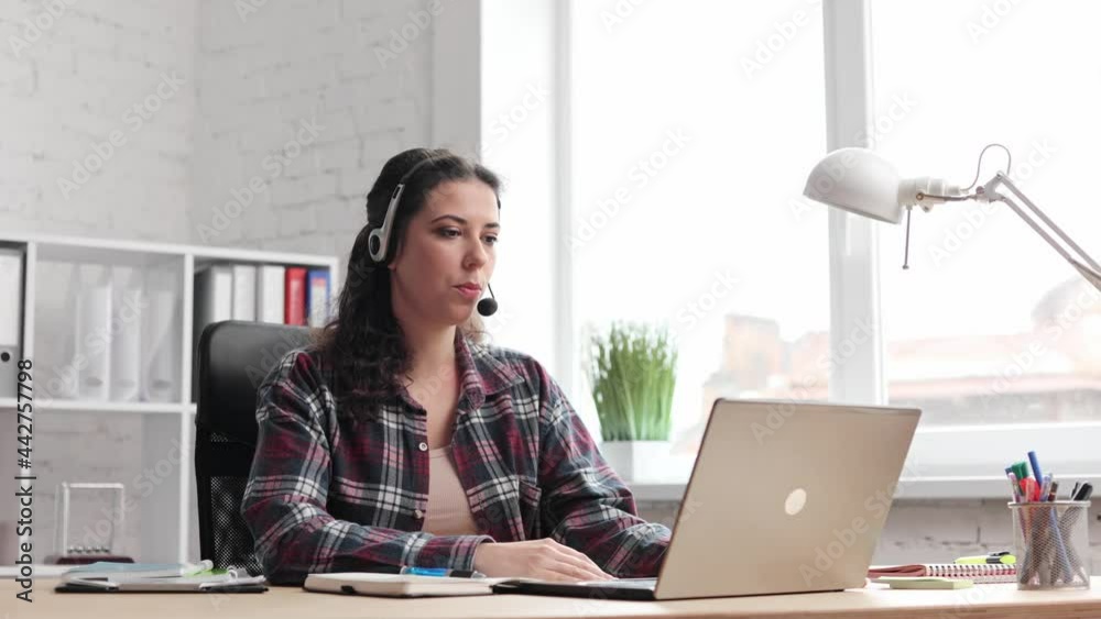 Girl internet teacher doing distant chat working. Close up. Smilimg young business female wears headset talks to web camera making distance online video conference call in office. Job interview. Girl internet teacher doing distant chat working. Close up. Smilimg young business female wears headset talks to web camera making distance online video conference call in office. Job interview.