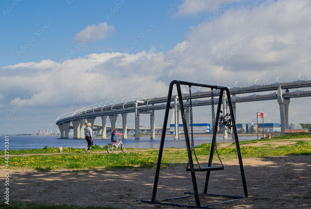 Fototapeta premium provincial village is swayed by the wind against the background of large round highway bridge in the blue sea and sky with clouds. People, leisure, concept past and future building world