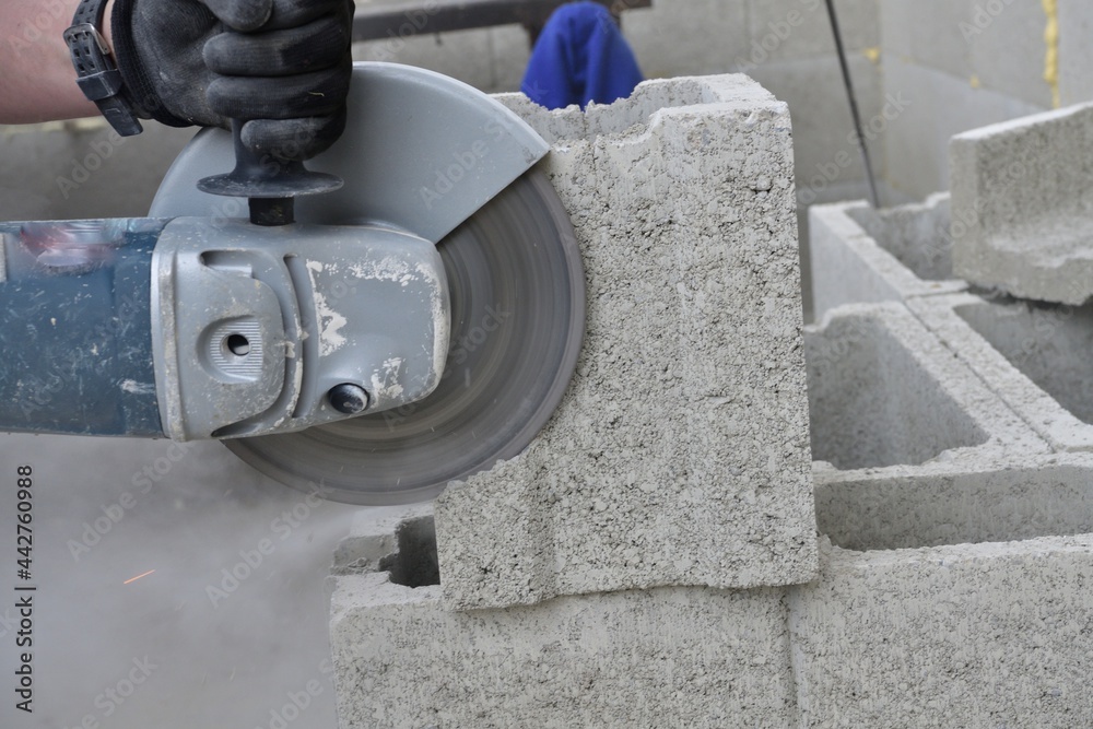 View of a mason's hands on a construction site sawing a block using an electric grinder