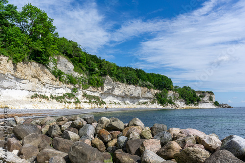 beautiful ocean landscape with steep white chalkstone cliffs and forest and rocks in the foreground