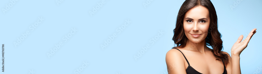 Obraz premium Portrait of smiling beautiful woman in black casual tank top, isolated over bright blue background. Brunette girl at studio. Beauty concept. Wide horizontal composition image with copy space area.
