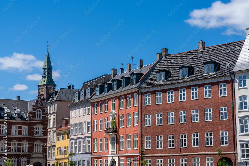 colorful historic cityscape and buildings with a church spire in the background under a blue sky with white cumulus clouds