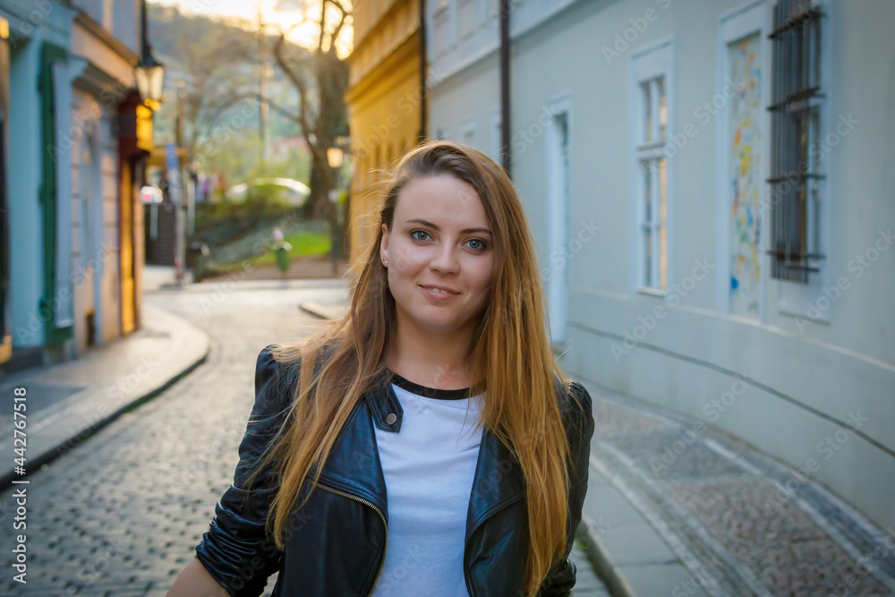 Fototapeta premium A young girl with long hair is walking along the city street. The road is paved with cobblestones.
