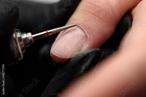 Professional hardware manicure on an electric machine in a nail salon. The process of lifting the cuticle with a cutter close-up. Master uses an electric nail file drill to trim and remove cuticles. photo
