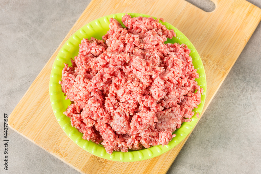 Chopped minced meat in a green plastic plate on a wooden cutting board. View from above. Chopped minced meat in a green plastic plate on a wooden cutting board. View from above.