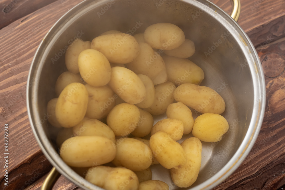 Freshly cooked young small potatoes in a saucepan with steam on a wooden background.