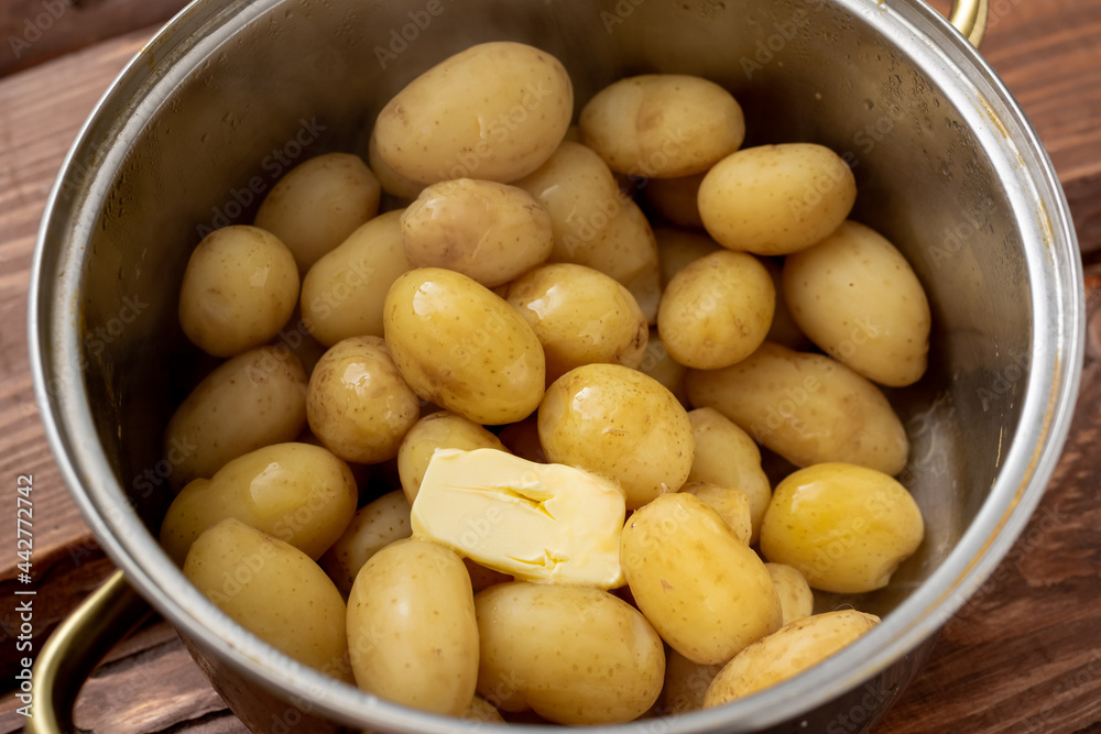 Freshly cooked young small potatoes in a saucepan with butter on a wooden background. Freshly cooked young small potatoes in a saucepan with butter on a wooden background.
