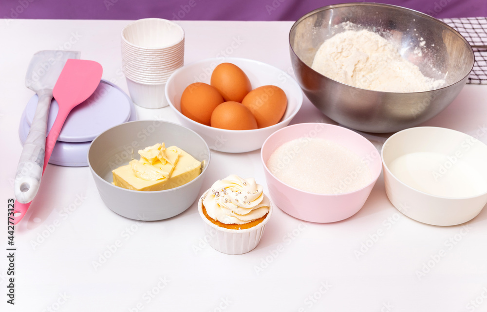 Ingredients and part of the equipment with a ready-made cake for making cupcakes on a white background. Flour, sugar, eggs, butter, spatulas, scales, milk. Selective focus. Ingredients and part of the equipment with a ready-made cake for making cupcakes on a white background. Flour, sugar, eggs, butter, spatulas, scales, milk. Selective focus.