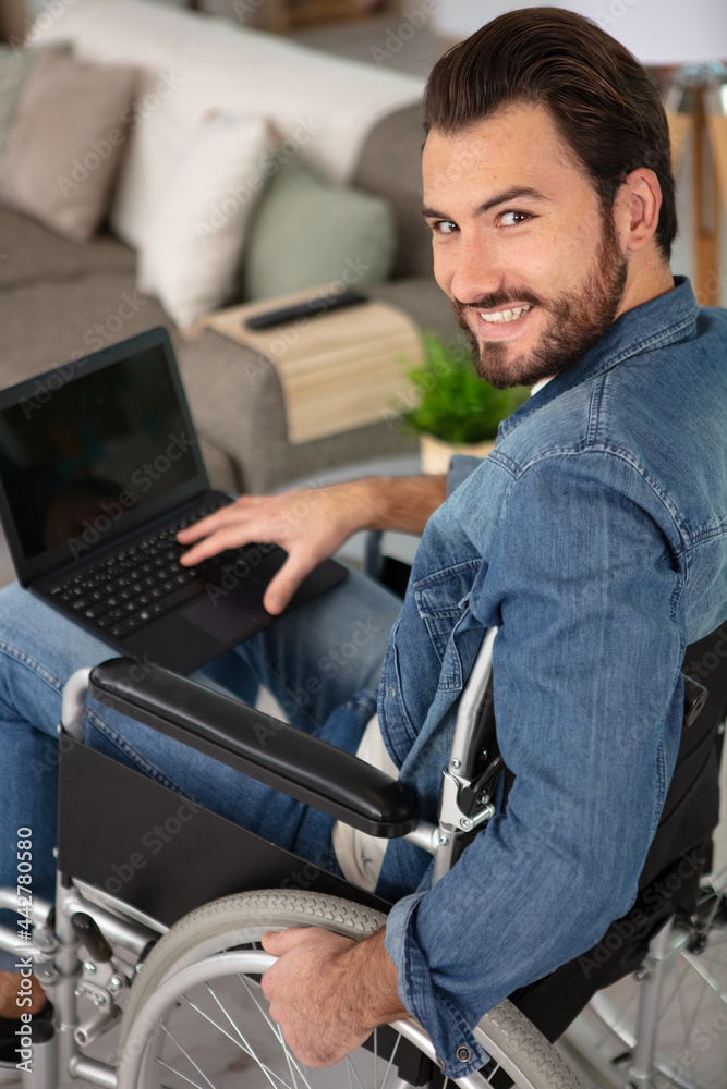 young man sitting in wheelchair using laptop at home young man sitting in wheelchair using laptop at home