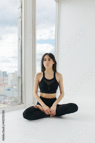 pretty armenian woman meditating in lotus pose on white floor near window