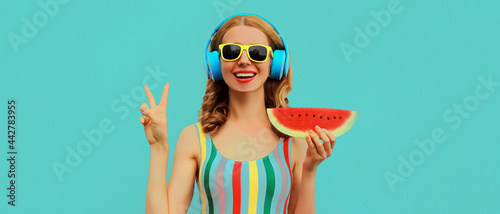 Summer colorful portrait of cheerful happy smiling young woman model posing in headphones listening to music with juicy slice of watermelon on a blue background