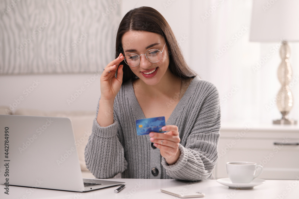 Woman with credit card using laptop for online shopping at white table indoors Woman with credit card using laptop for online shopping at white table indoors