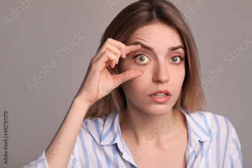 Woman checking her health condition on grey background. Yellow eyes as symptom of problems with liver
