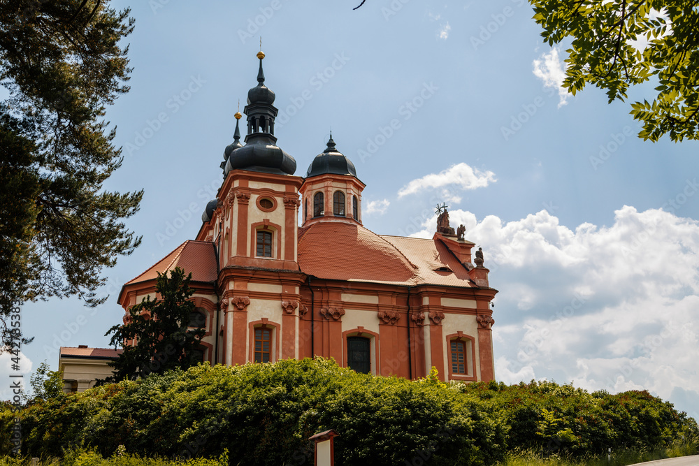 Valec, Western Bohemia, Czech Republic, 19 June 2021:  Baroque red and yellow church of the Holy Trinity with towers near castle at summer sunny day