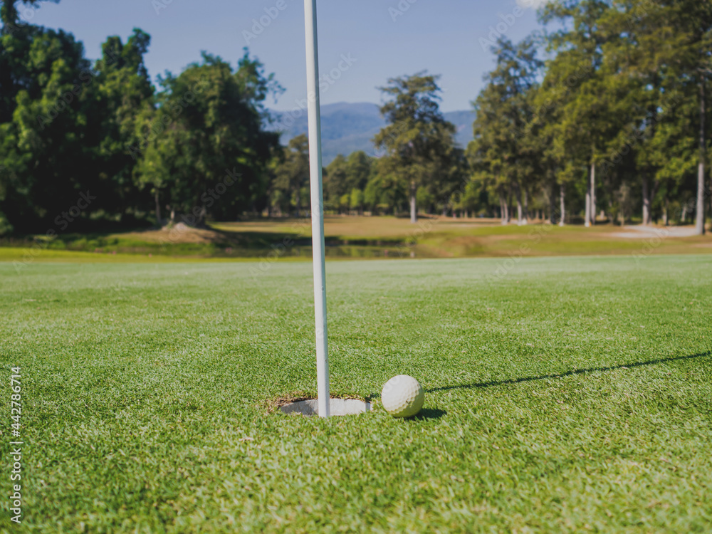 Obraz premium Photo of white golf ball on grass with hole and blue sky background