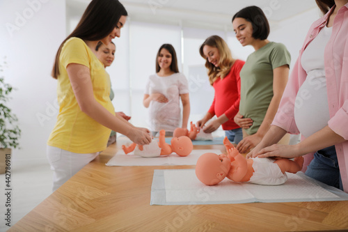 Pregnant women learning how to swaddle baby at courses for expectant mothers indoors, closeup photo