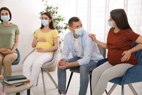 Pregnant women and man with protective masks at courses for expectant parents indoors photo