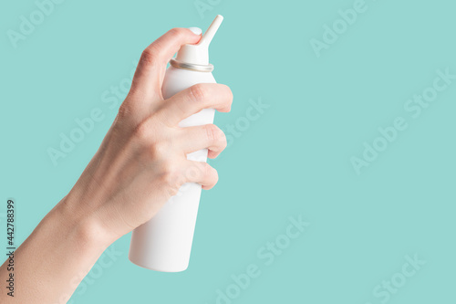 spray bottle with salt sea water for nasal cavity hygiene in female hand isolated on turquoise background