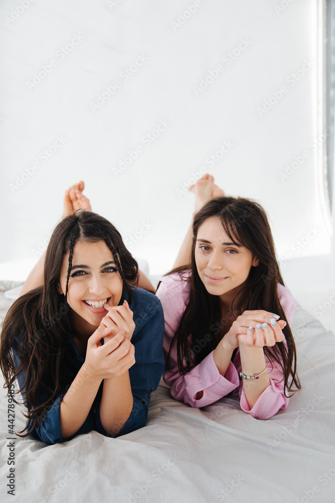 young and happy armenian women smiling at camera while lying on white bedding young and happy armenian women smiling at camera while lying on white bedding