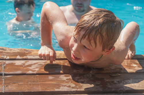 Fotografie A wet boy gets out of the pool water after swimming on a hot summer day