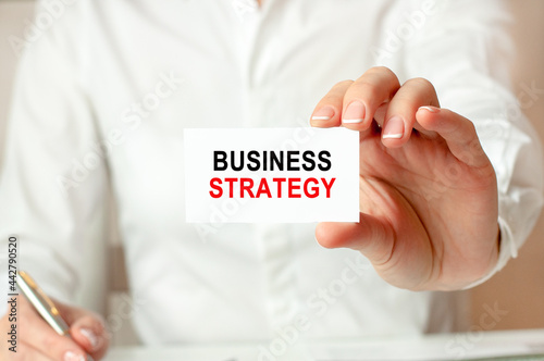 a woman in a white shirt holds a piece of paper with the text: BUSINESS STRATEGY. Business concept.