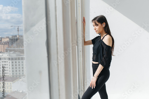 sportive armenian woman in earphone and sportswear dreaming near window
